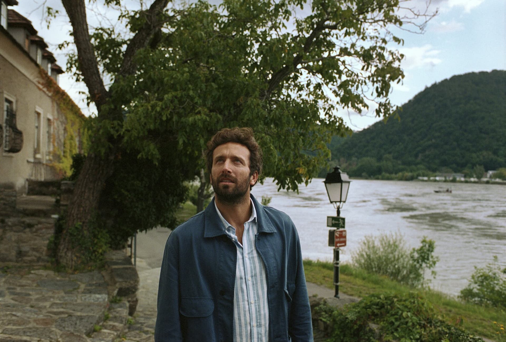 Man standing beneath tree around river bank and house