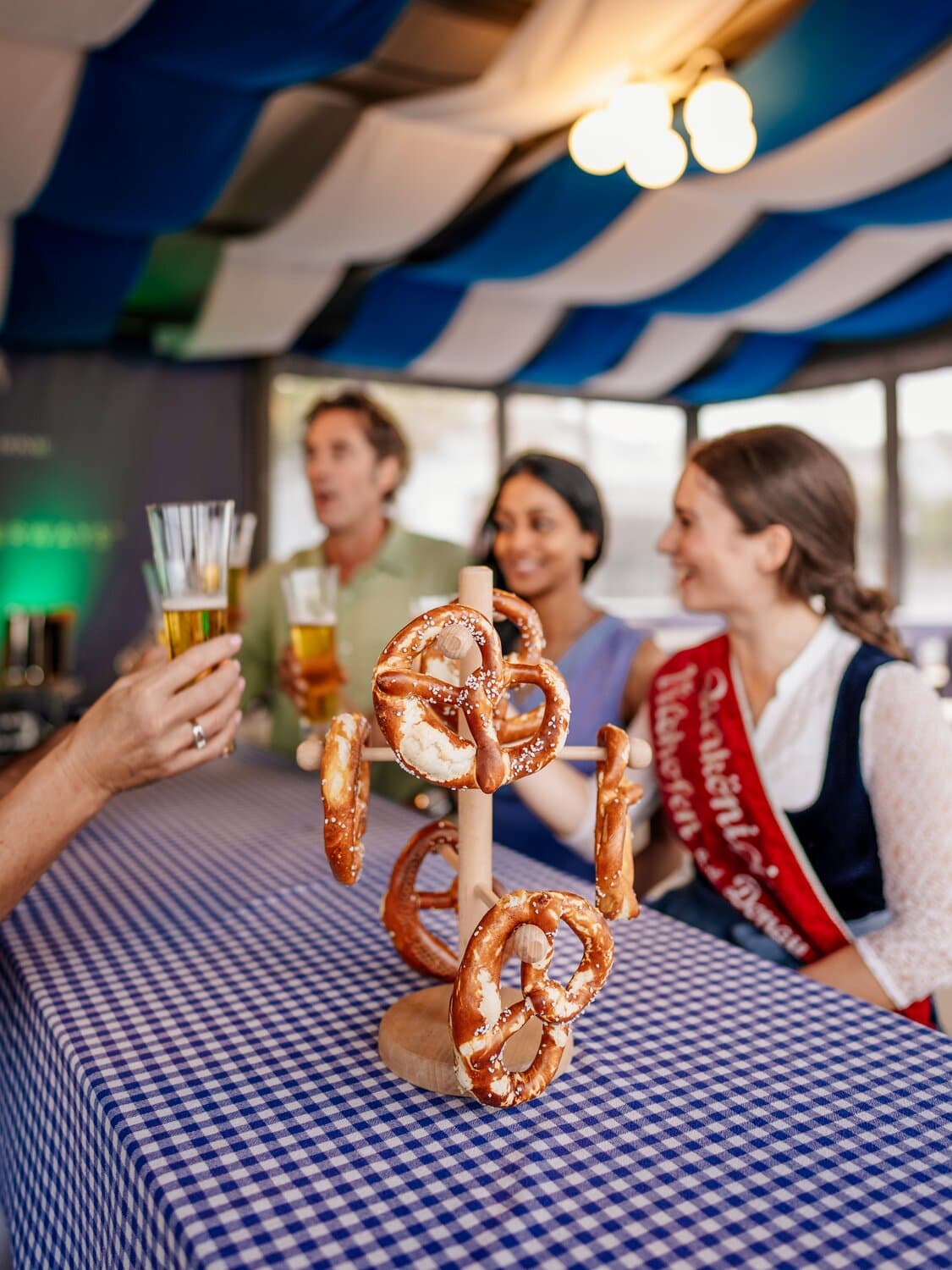 A group of people sitting at a table drinking beer with a pretzel display in the middle